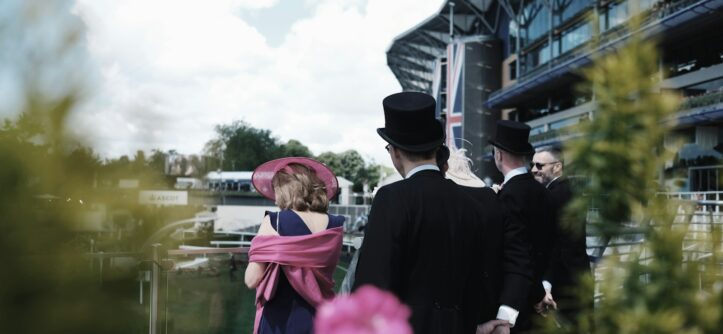 Racegoers in smart suits and a pink hat in the audience at Royal Ascot